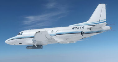 A white plane carrying the AgilePod case that contains L3Harris' IRST system with a clear sky background