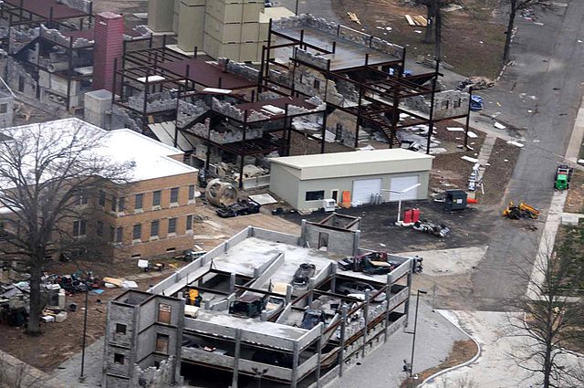 Aerial view of buildings damaged after a dirty bomb explosion, showing structural debris and emergency response vehicles on site