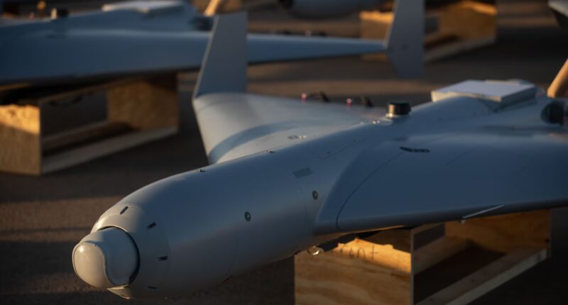 Close-up view of a LUCAS drone resting on a wooden stand, showing its sleek fixed-wing design and nose-mounted sensor under warm evening light.