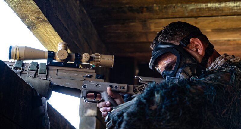 Soldier wearing protective goggles aims a sniper from inside a concrete fighting position during a military training exercise