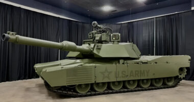 M1E3 Abrams main battle tank displayed indoors, showing its upgraded turret, long main gun, reinforced armor, and U.S. Army markings under exhibition lighting.