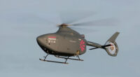 A small autonomous helicopter flying through the air against a clear blue sky.