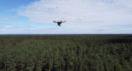 A drone surveys a dense forest under a partly cloudy sky, showcasing how drones can assist in radioactive recovery during daylight hours.