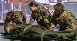 U.S. military personnel in OCP camouflage uniforms practicing trauma simulation casualty care on a litter during an indoor training exercise