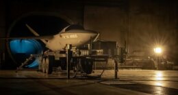 Kratos XQ-58 Valkyrie stealth drone displayed on a wheeled trailer inside a military hangar during low-light pre-flight or testing operations, co-branded with Airbus