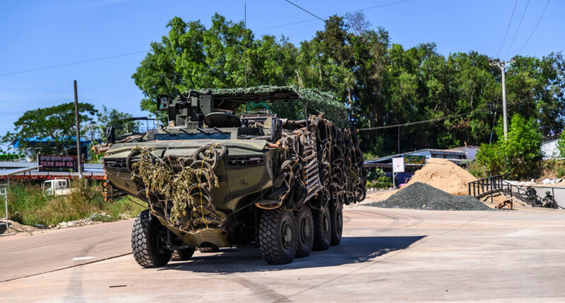 Royal Thai Navy amphibious 8x8 armored vehicle draped in camouflage netting and tire armor moving along a road during border defense operations