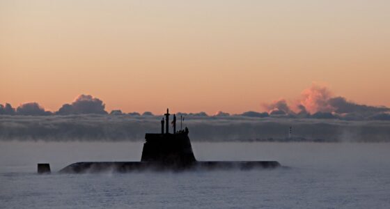 A military submarine emerges through dense sea mist under a dramatic orange dawn sky, used to illustrate Indra's development of a new satellite link to extend submarine connectivity at sea