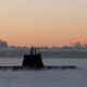 A military submarine emerges through dense sea mist under a dramatic orange dawn sky, used to illustrate Indra's development of a new satellite link to extend submarine connectivity at sea