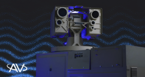 AV laser weapon system featuring a dual-aperture directed energy turret with blue accent lighting, mounted on a ground equipment stack against a dark particle-wave graphic background