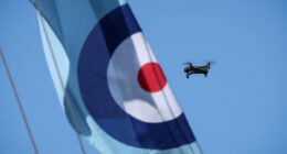 A compact quadcopter drone in flight alongside a Royal Air Force roundel banner during Exercise Agile Warrior, used to illustrate advances in quantum-resilient drone navigation and communications
