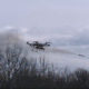 Serbian military autonomous quadcopter drone firing an aircraft rocket with a smoke plume trailing behind it over a bare winter treeline, showcasing the platform's multi-rocket air-to-ground strike capability