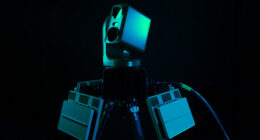 Roke counter-drone system featuring a multi-sensor turret head and flanking electronics modules on a tripod mount against a dark background